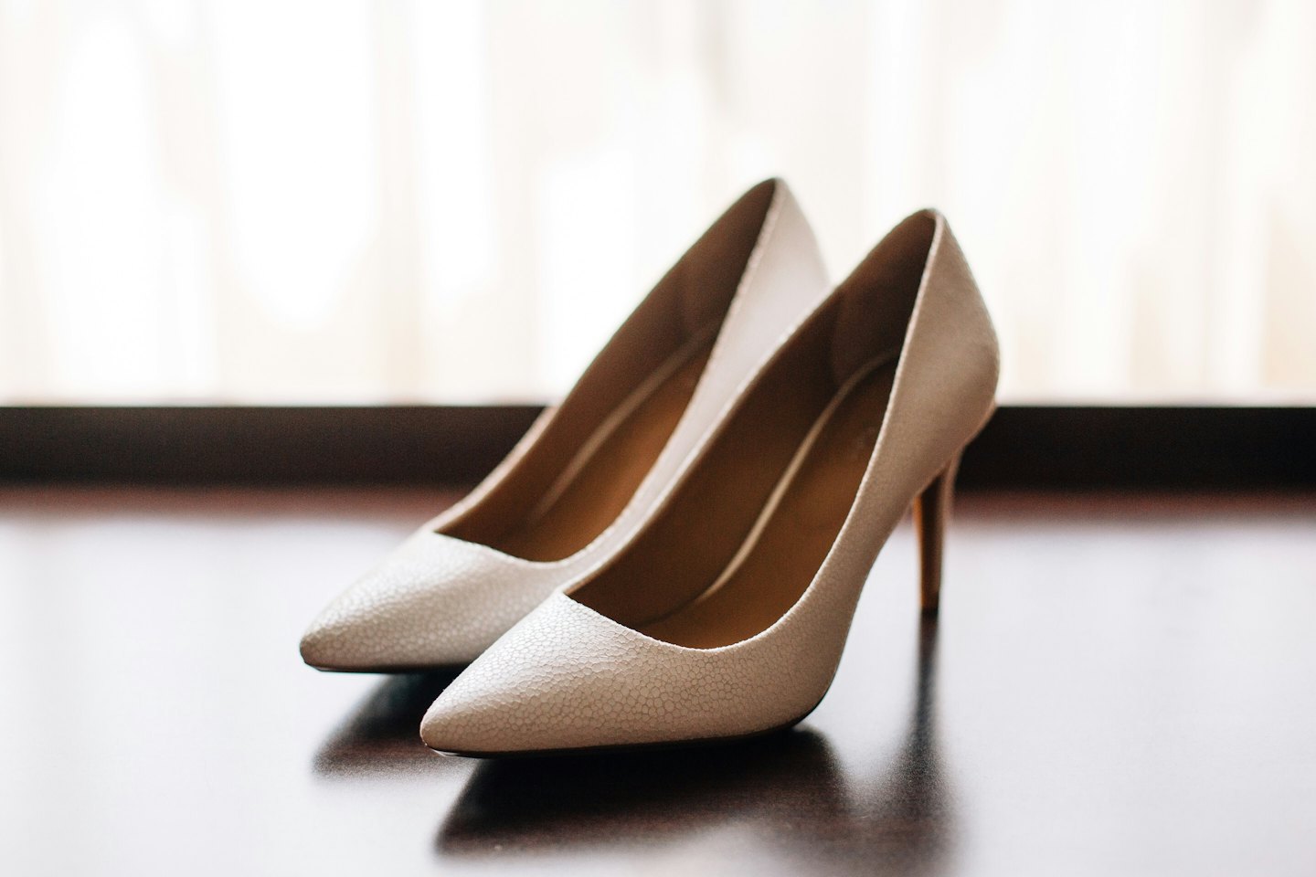 Eleganti scarpe con tacco alto color chiaro su una superficie lucida.